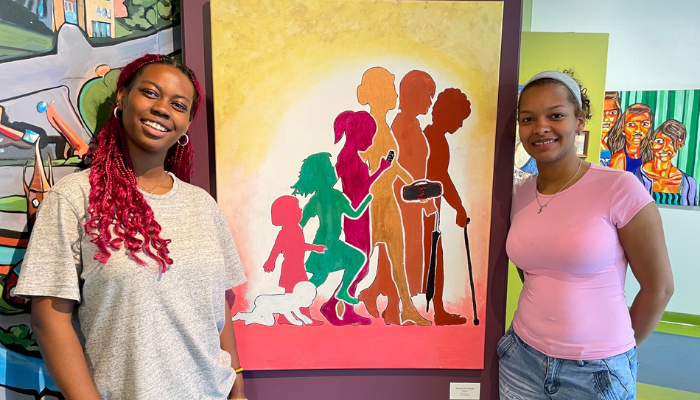 Two people smiling next to a painting.