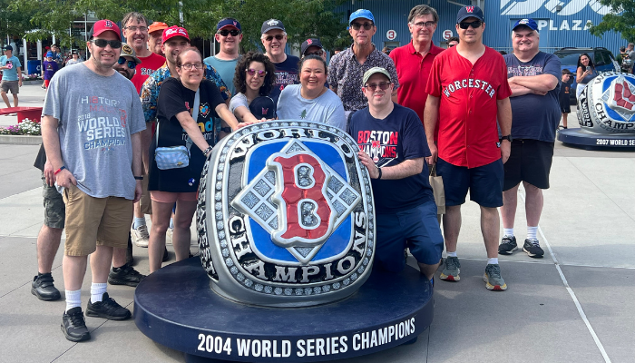 A group of individuals gathered around a statue of a Boston Red Sox World Series Championship ring.