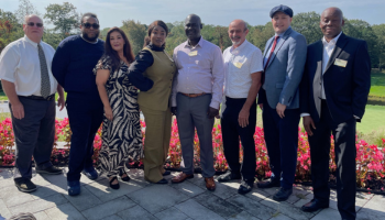 A picture of 8 people standing together dressed nicely for luncheon